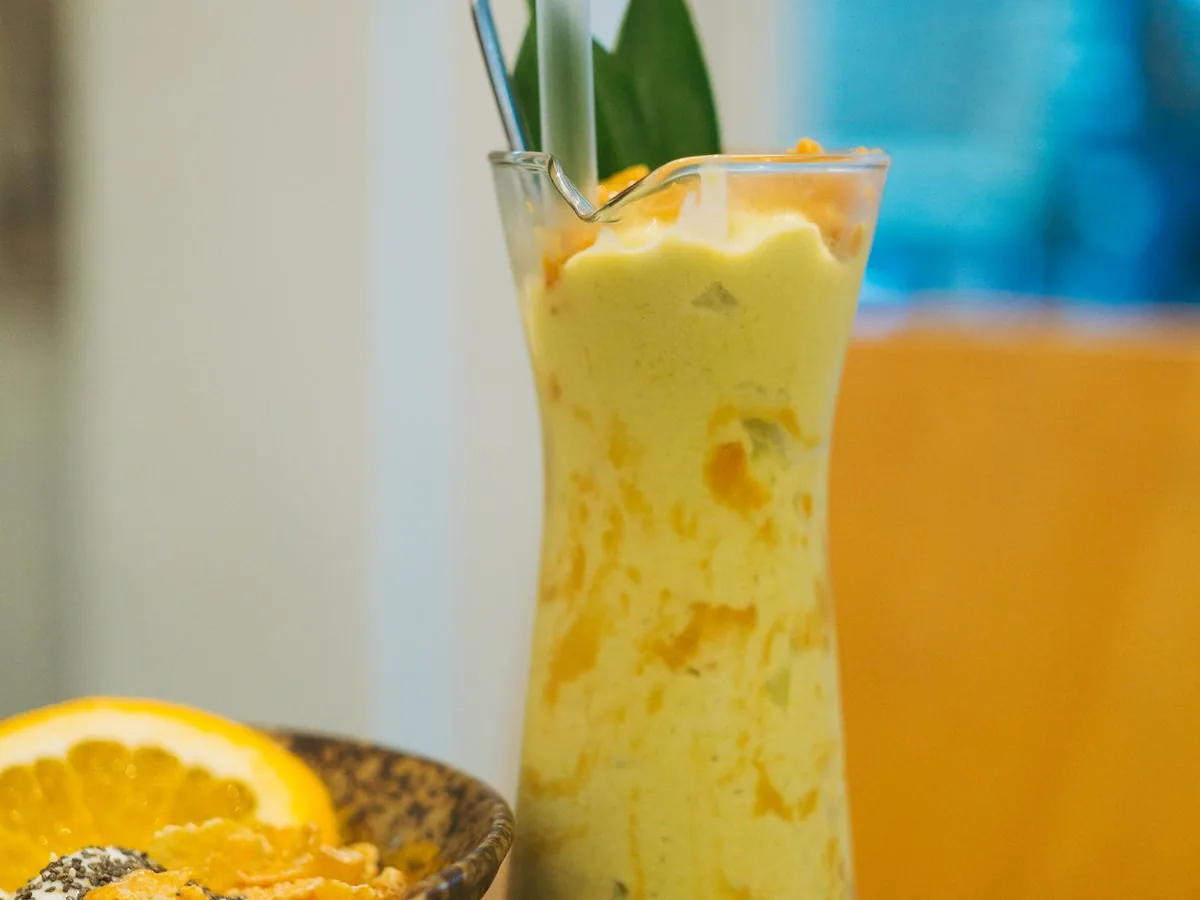 Högt glas med krämig orange smoothie och en apelsinskiva på kanten